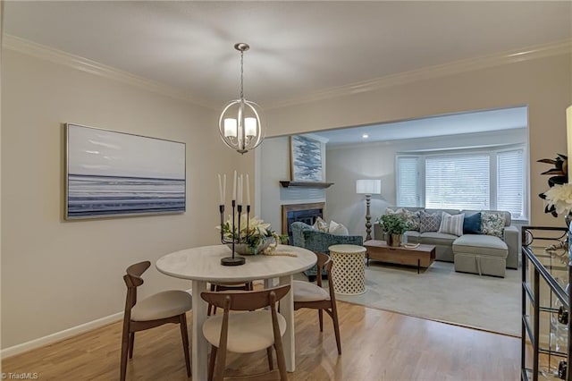 dining area featuring light wood-type flooring, ornamental molding, a chandelier, a fireplace, and baseboards