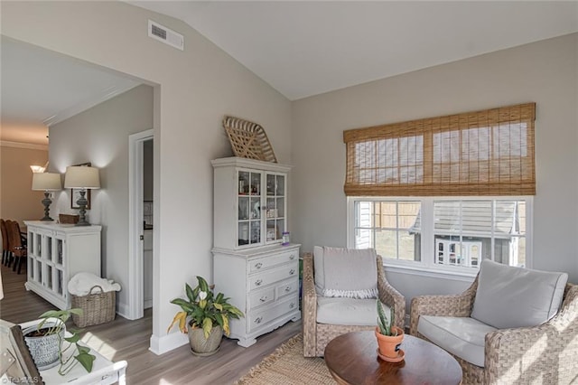 living area with vaulted ceiling, wood finished floors, visible vents, and baseboards