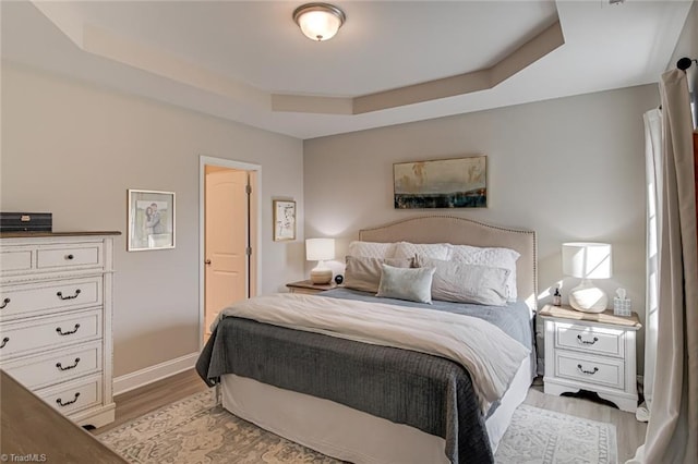 bedroom with light wood-type flooring, baseboards, and a tray ceiling