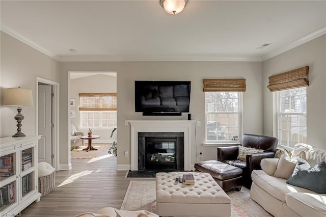 living area featuring visible vents, light wood-style flooring, ornamental molding, a fireplace with flush hearth, and baseboards