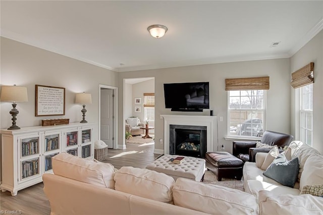 living area featuring light wood-style floors, a glass covered fireplace, and ornamental molding