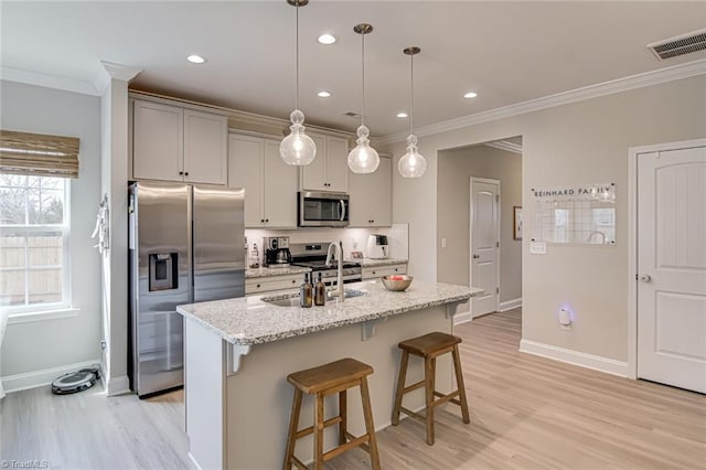 kitchen featuring crown molding, stainless steel appliances, visible vents, a sink, and a kitchen breakfast bar