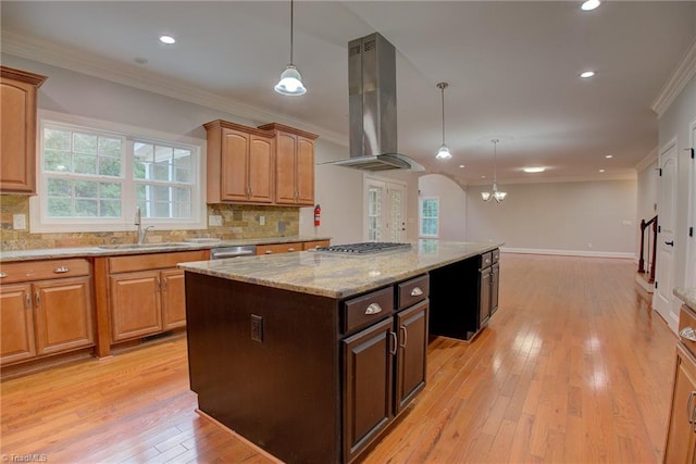 kitchen with light wood-type flooring, backsplash, a kitchen island, ventilation hood, and light stone countertops