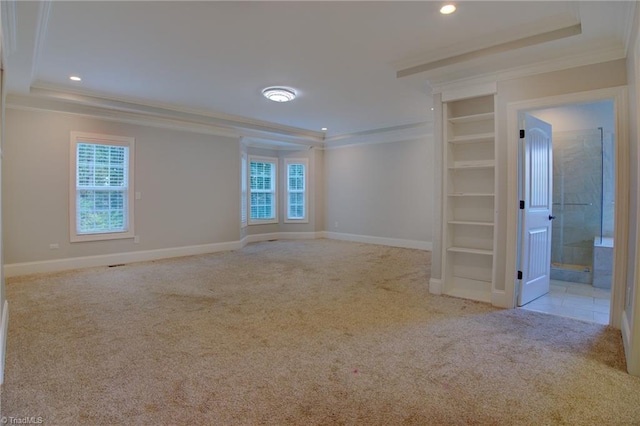 empty room featuring built in shelves, ornamental molding, light colored carpet, and a tray ceiling