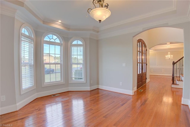 unfurnished room with a notable chandelier, ornamental molding, a raised ceiling, and hardwood / wood-style floors