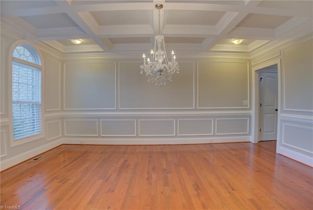 empty room featuring a notable chandelier, coffered ceiling, light wood-type flooring, and a healthy amount of sunlight