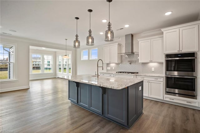 kitchen with double oven, white cabinets, wall chimney exhaust hood, and decorative light fixtures