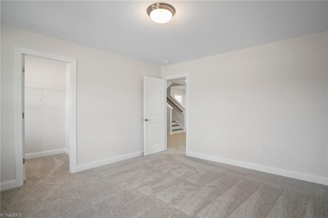 unfurnished bedroom with a walk in closet, a closet, and light colored carpet