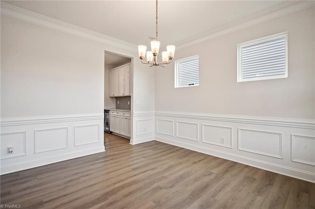 unfurnished room featuring wood-type flooring, an inviting chandelier, and ornamental molding