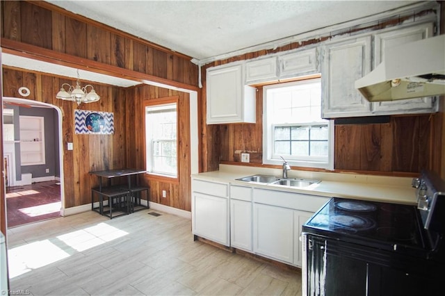 kitchen featuring white cabinetry, electric range, wooden walls, a healthy amount of sunlight, and decorative light fixtures