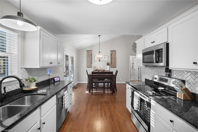 kitchen with lofted ceiling, decorative light fixtures, stainless steel appliances, white cabinetry, and a sink