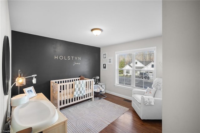 bedroom with a nursery area, visible vents, dark wood finished floors, and baseboards