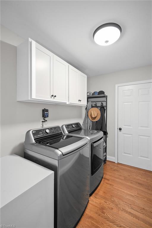 clothes washing area with cabinet space, washing machine and dryer, and light wood-style floors