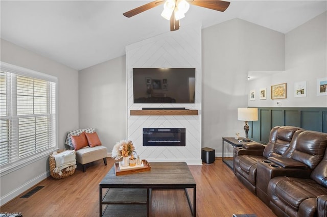 living area featuring lofted ceiling, a large fireplace, visible vents, and light wood-style flooring