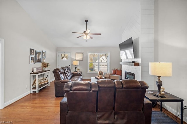 living room featuring baseboards, ceiling fan, wood finished floors, vaulted ceiling, and a high end fireplace