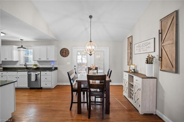 dining room with dark wood-style floors, a chandelier, vaulted ceiling, and baseboards