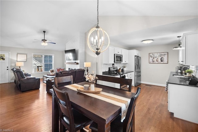 dining area featuring lofted ceiling, ceiling fan with notable chandelier, dark wood-style floors, and baseboards