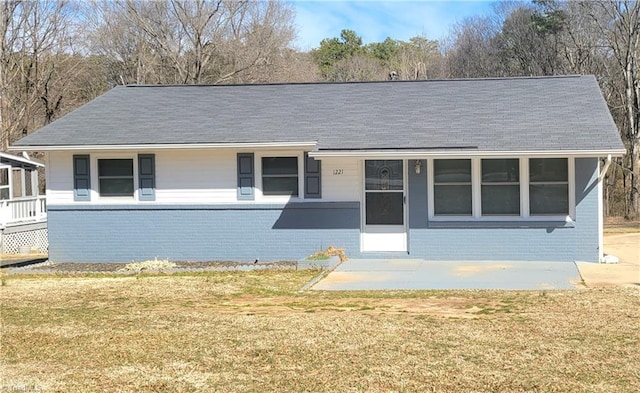 single story home featuring a patio area, roof with shingles, a front yard, and brick siding