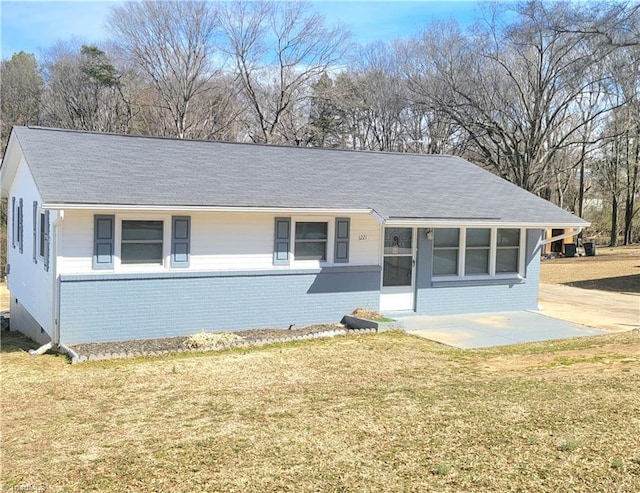 ranch-style home with roof with shingles, a front yard, a patio, and brick siding