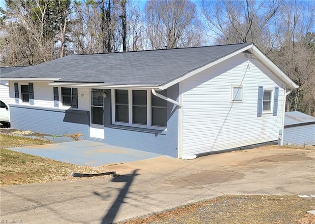 ranch-style house featuring driveway, a shingled roof, a porch, and brick siding