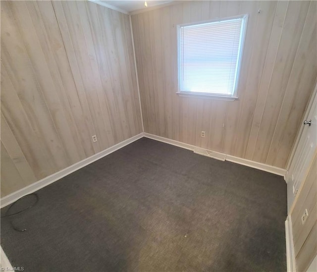 spare room with dark carpet, wooden walls, and baseboards