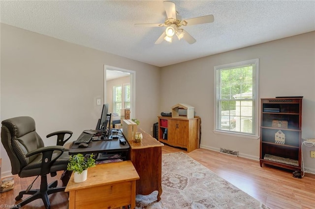 office area with a wealth of natural light, visible vents, light wood-type flooring, and ceiling fan