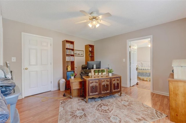 office featuring baseboards, a textured ceiling, light wood-style flooring, and a ceiling fan