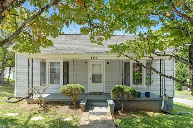 view of front of property with roof with shingles, covered porch, and a front yard