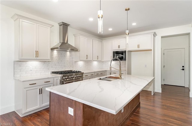 kitchen featuring dark hardwood / wood-style flooring, wall chimney exhaust hood, hanging light fixtures, an island with sink, and high end stove