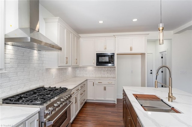 kitchen featuring high end stainless steel range oven, black microwave, sink, wall chimney range hood, and decorative light fixtures