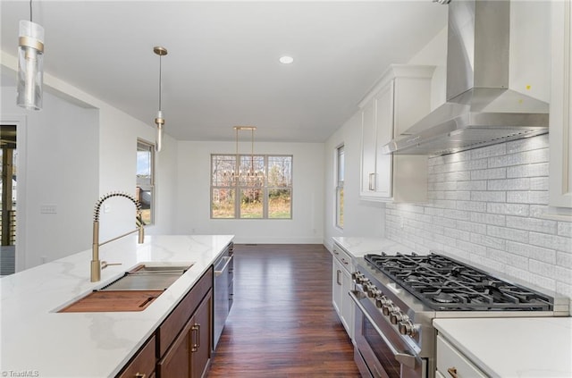 kitchen featuring stainless steel appliances, sink, wall chimney exhaust hood, dark hardwood / wood-style floors, and decorative light fixtures