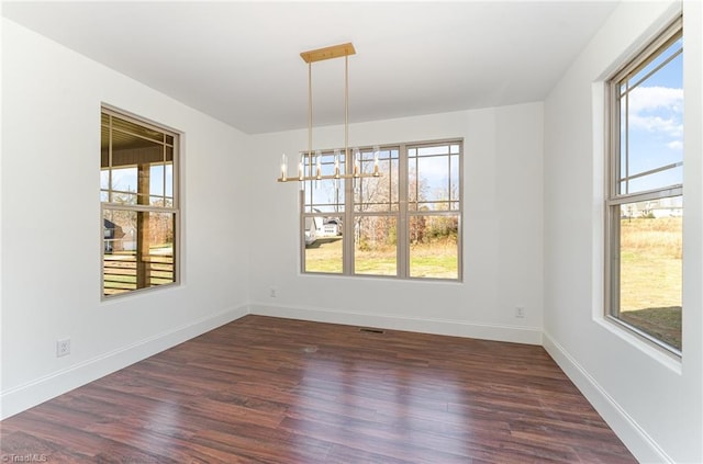 unfurnished dining area with a wealth of natural light, dark hardwood / wood-style floors, and a chandelier