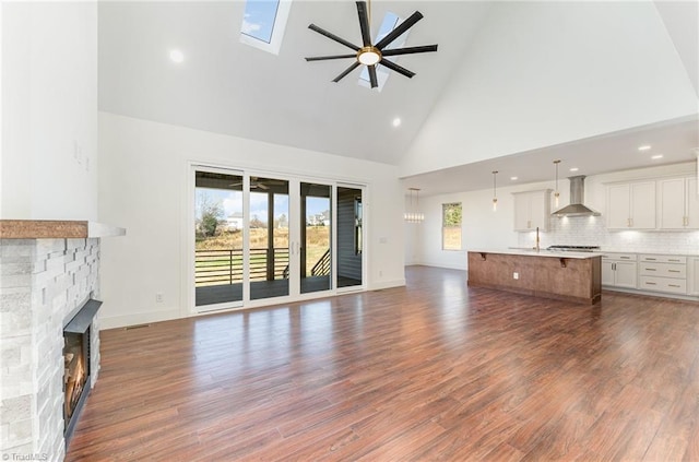 unfurnished living room with a stone fireplace, dark hardwood / wood-style floors, high vaulted ceiling, a skylight, and ceiling fan