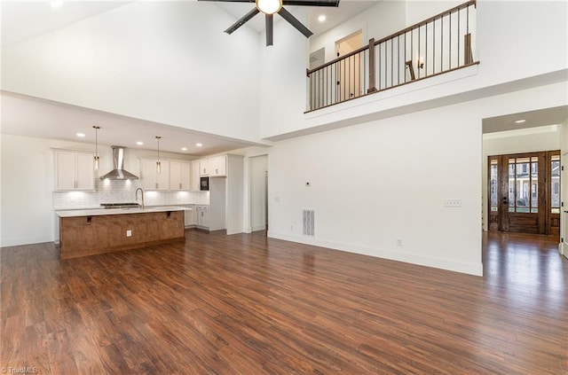 unfurnished living room featuring a towering ceiling, dark hardwood / wood-style floors, and ceiling fan