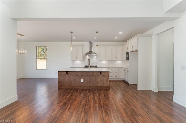 kitchen featuring white cabinets, hanging light fixtures, a kitchen island with sink, dark hardwood / wood-style floors, and wall chimney range hood