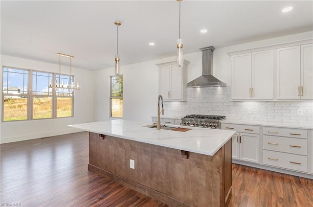 kitchen featuring a kitchen island with sink, wall chimney exhaust hood, pendant lighting, and light stone countertops