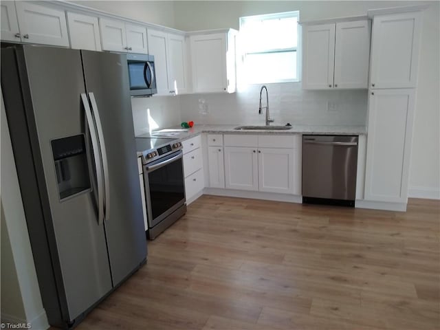 kitchen featuring backsplash, stainless steel appliances, light wood-style floors, white cabinetry, and a sink