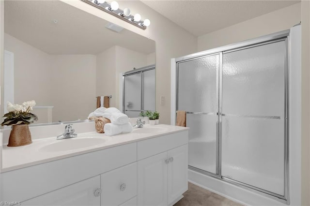 bathroom with vanity, a shower with shower door, and a textured ceiling