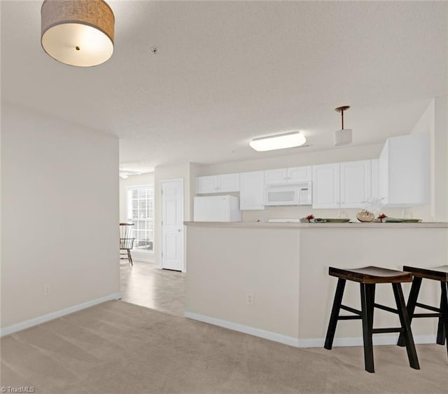 kitchen with kitchen peninsula, light carpet, a kitchen breakfast bar, white appliances, and white cabinetry