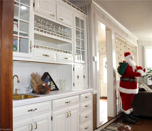 bar featuring white cabinets, backsplash, ornamental molding, and sink