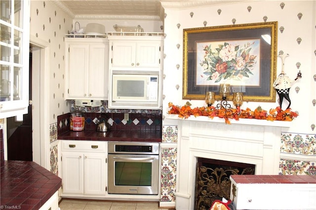 kitchen with tile counters, oven, decorative backsplash, white microwave, and ornamental molding