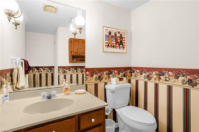 half bath with toilet, a wainscoted wall, and vanity