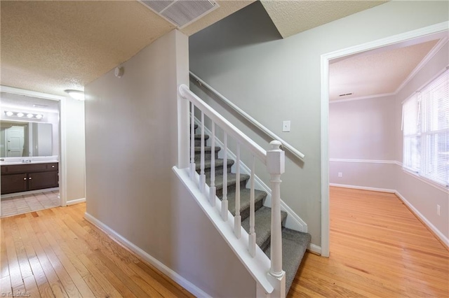 stairway with hardwood / wood-style floors, crown molding, and a textured ceiling