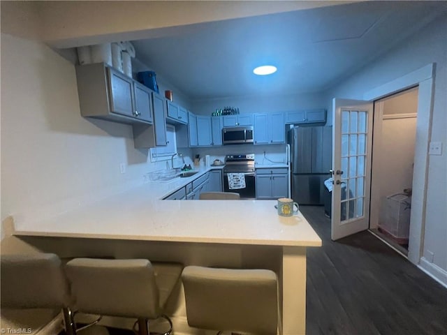 kitchen featuring sink, dark hardwood / wood-style floors, kitchen peninsula, a breakfast bar, and appliances with stainless steel finishes