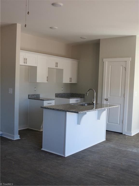 kitchen featuring sink, a center island with sink, dark stone countertops, dark hardwood / wood-style floors, and white cabinets