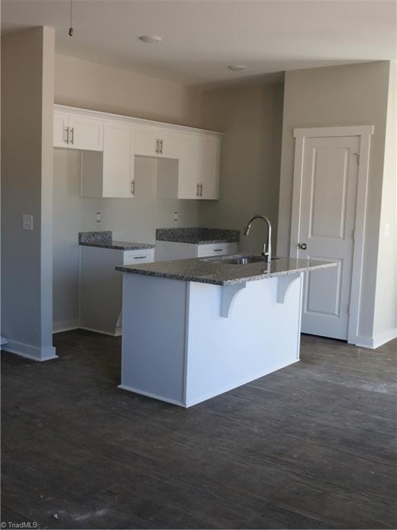 kitchen featuring a kitchen island with sink, sink, white cabinets, and stone counters