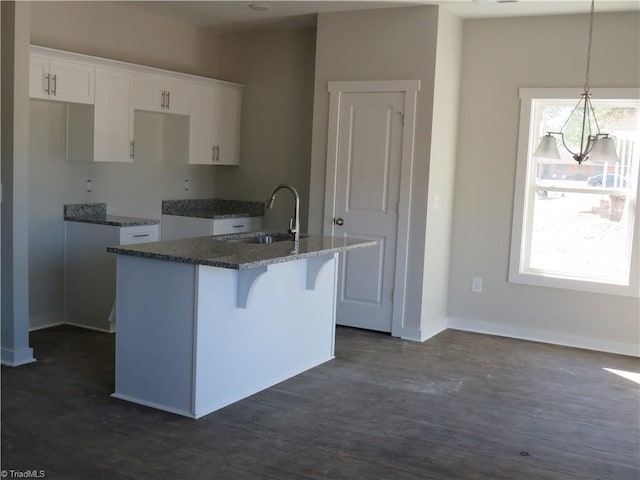 kitchen with sink, decorative light fixtures, dark stone countertops, an island with sink, and white cabinets