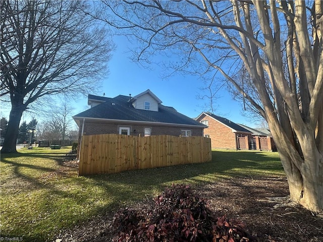 view of property exterior with brick siding, a lawn, and fence