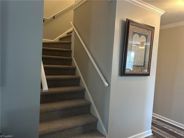 stairway with a textured ceiling, ornamental molding, wood finished floors, and baseboards