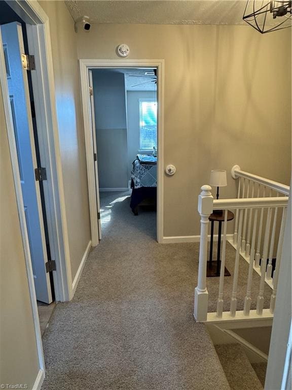 hall with carpet flooring, an upstairs landing, and baseboards